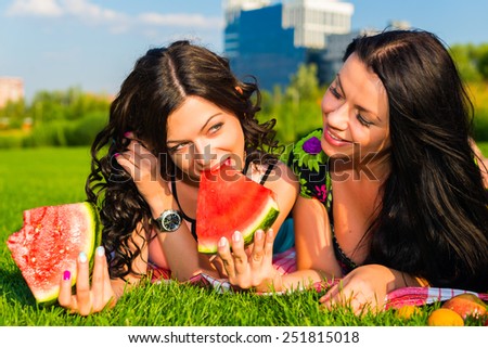 Two  young happy girlfriends picnicking on the lawn  on green grass  and enjoying watermelon.