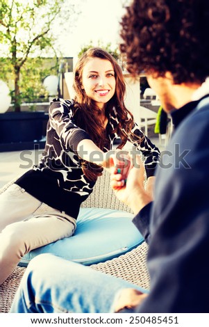 Pretty young woman flirting with her boyfriend holding hands and smiling into his eyes as they sit together outdoors, view over his shoulder
