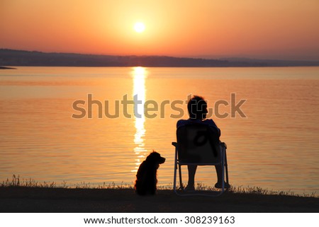 Man and his friend dog admire the sunrise at sea