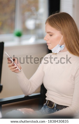 Female customer in beauty salon sitting on hight chair in medical mask on chin and use phone. Beautiful young blond hair woman wiating for brow master Zdjęcia stock © 
