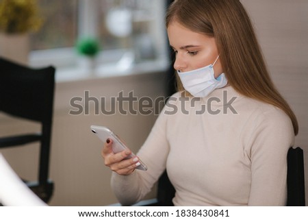 Female customer in beauty salon sitting on hight chair in medical mask and use phone. Beautiful young blond hair woman wiating for brow master. Open nose Zdjęcia stock © 