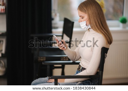 Female customer in beauty salon sitting on hight chair in medical mask and use phone. Beautiful young blond hair woman wiating for brow master. Open nose Zdjęcia stock © 