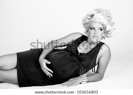 Beautiful pregnant woman with long curly blonde hair and a very large protruding belly lying in a black dress holding her stomach