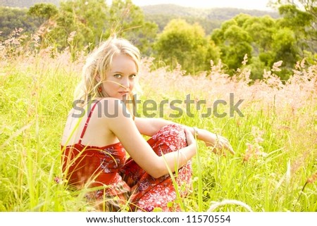 beautiful girl sitting in a grassy field in  the afternoon sun