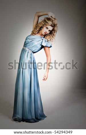 Portrait of a young woman. Her hair is wild and she is wearing a blue dress which is off one shoulder. Vertical shot. Isolated on white.
