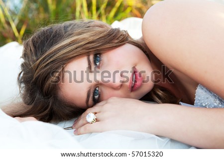 An attractive young woman with a slight smile is lying down in a field of grass. Horizontal shot.