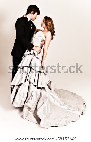 A young couple dressed in formal attire dancing affectionately with the man\'s arm around the woman\'s waist. The woman is wearing a white strapless dress and the man is wearing a suit. Vertical shot.