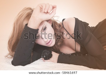 Sensual young female wearing black lingerie is lying on her side on a white bed. She is shot through a filtered lens. Horizontal shot.