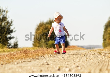 A little girl Ina floppy hat standing on a gravel road,