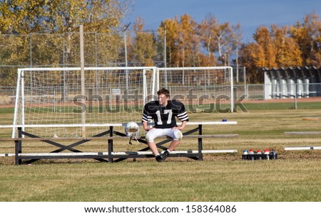 A boy in a football equipment sitting on a bench