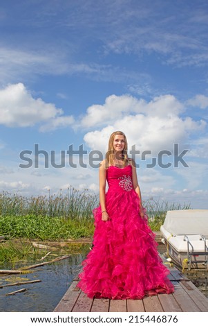 Girl in red prom dress standing on boat dock