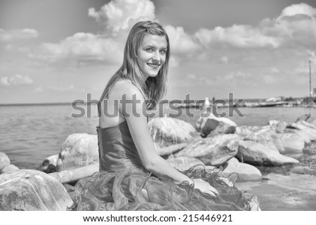 Girl in prom dress sitting on rocks at lake