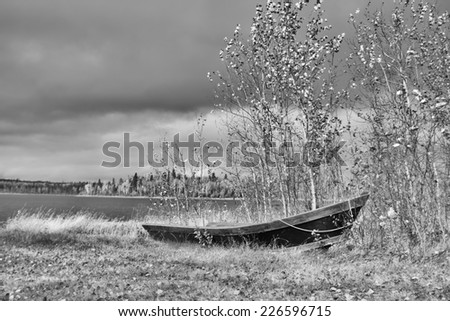Old wooden canoe beached by lake in black and white