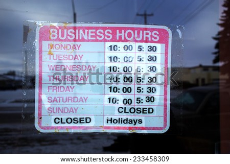 Plastic sign hanging in window announcing weekly store hours