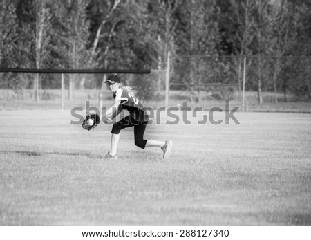 A teenage girl running and catching a baseball in her glove in black and white
