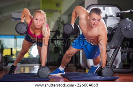 Gym man and woman push-up strength pushup with dumbbell in a fitness workout