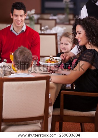 Waiter serving a family in a restaurant and bringing a full plate