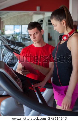 Trainer explains to a young woman how to use treadmill in fitness club