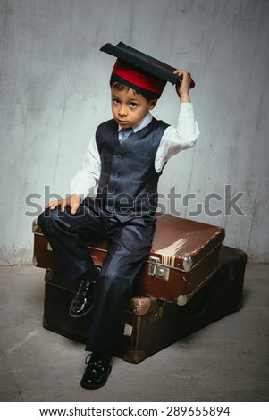small black boy in suit and graduation hat sits on the old suitcases and look left. instagram toned