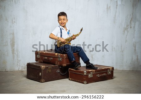 six years old boy sit with saxophone on old suitcases. instagram toned