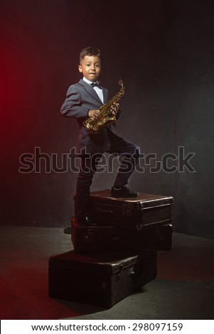 six years old boy stand with saxophone on old suitcases. instagram toned