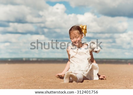 Pretty little girl sit at the sand on the beach at wind weather,.