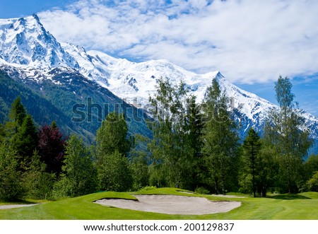 Golf field with sand bunkers over snow covered Alps.