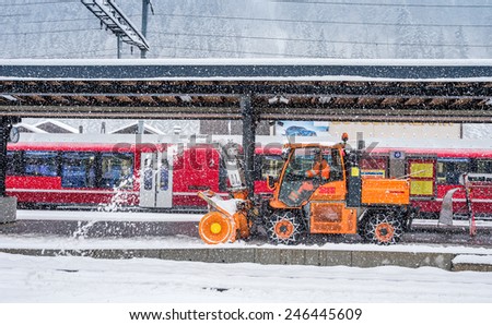 Snow cleaning machine over red train at Klosters, Switzerland train station during strong snow fall.