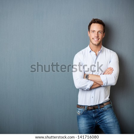 Portrait of a smart young man standing with arms crossed against gray background