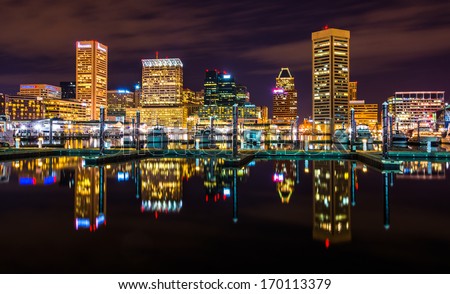 The skyline and docks reflecting in the water at night, in the Inner Harbor of Baltimore, Maryland.
