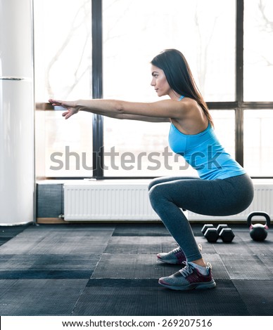 Side view portrait of a young woman doing squats at fitness gym