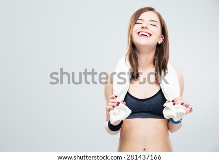 Portrait of a happiness laughing fitness woman with towel standing over gray background. 