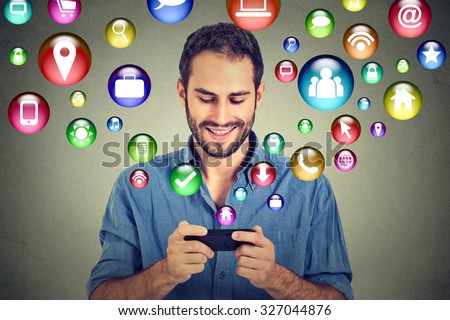 communication technology mobile phone high tech concept. Happy man using texting on smartphone social media application icons flying out of cellphone isolated grey wall background. 4g data plan