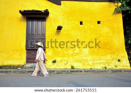 HOI AN, VIETNAM - MARCH 13: Old woman goes by the street in historical centre of Hoi An, Vietnam on March 13, 2015. Hoi An is the city recognized as a World Heritage Site by UNESCO.