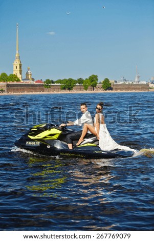02.06.2013, Russia, Saint-Petersburg: Newlyweds go on jet skis, the bride and groom on the background of Peter and Paul Fortress, the water area of the Neva river, boat, beach, blue sky, sunny weather