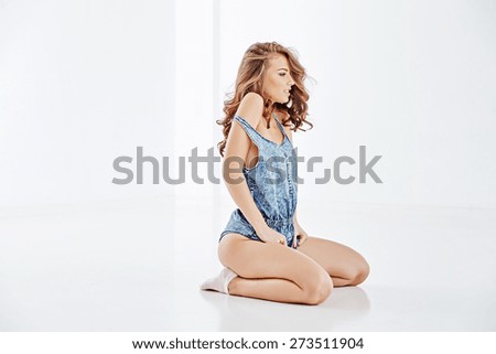 Beautiful girl sits on a glossy white floor in a white room, dressed her short blue suit, pink socks, her curly hair, beautiful eyebrows