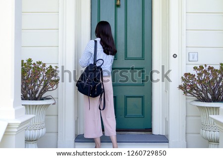 back view of girl college student carrying backpack back to home using key opening door. young office lady from work unlock house to enter the room. two plants beside front door in white wooden house