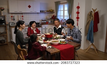 happy asian extended family laughing at the man's joke while having reunion dinner on chinese new year's eve in a cozy festive home interior