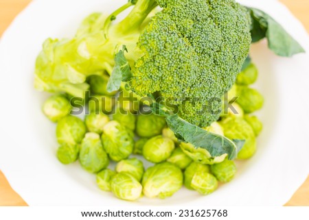 Raw broccoli and brussels sprout in a white plate on the kitchen table washed and ready for cooking