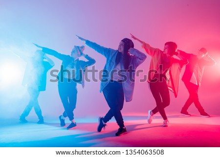 Young modern dancing group of six adult young people practice dancing on colorful background. Fashionably dressed youngsters moving over blurred disco club color lights Foto stock © 