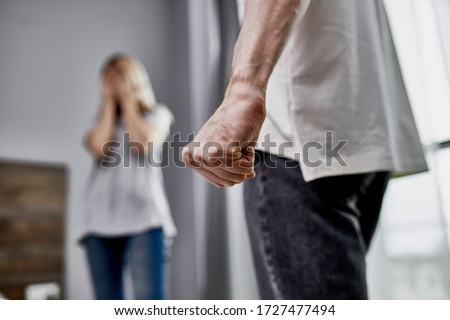 close-up photo of male fist, angry man and scared woman in the background, she close her face with hands. at home