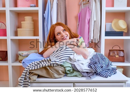 young redhead attractive caucasian woman happy positive smile hold credit card buy purchase clothes shopper sit behind table with outfits at home in cozy bright room, shopaholic. consumerism concept Сток-фото © 