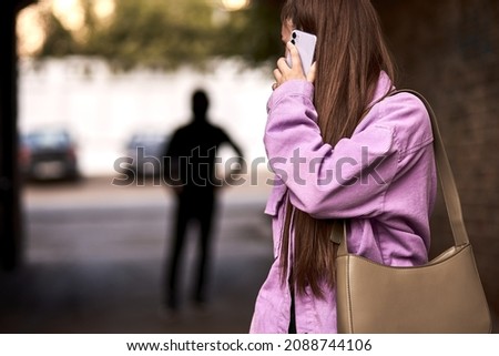 Criminal stalking woman, commiting crime while victim was walking alone, talking on phone in dark street. Caucasian young woman is looking back, afraid of male stranger person in the background Stock foto © 