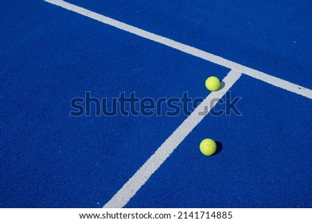 Foto Bild Zwei Bälle neben den Aufschlaglinien auf einem blauen Paddle-Tennisplatz.