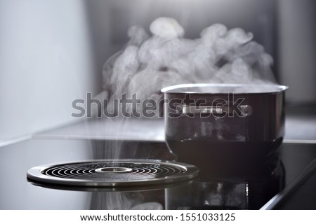 Modern electric induction cooker with built-in ventilation and extractor hood which draws steam from boiling water in a pan. Steam from a boiling pot is drawn into the integrated range hood Сток-фото © 
