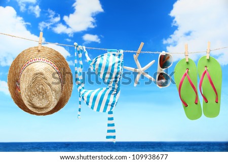 Women's swimsuit, hat and flip-flops hanging on a rope near beach.