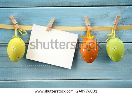 Easter eggs hanging on wood background with blank card.
