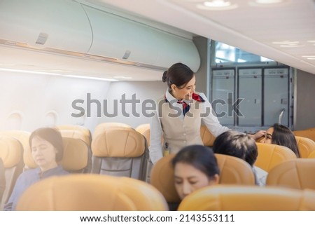 Beautiful female flight attendants checking the passengers on safety standard, seat belt, turn off electric devices, seat back and tray table in upright position before airplane take off and landing. Сток-фото © 