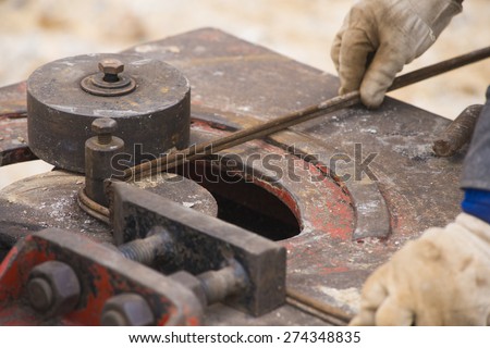 close-up worker hands bending concrete reinforcing metal rods by bender equipment
