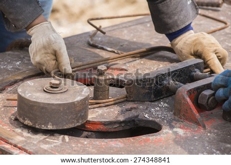 close-up worker hands bending concrete reinforcing metal rods by bender equipment
